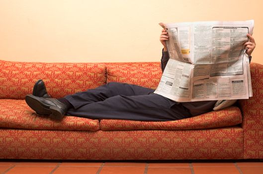Businessman reading newspaper whilst waiting for appointment corporate office and lying on sofa
