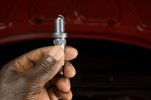 South African or American mechanic with spark plug and engine maintenance repair car background