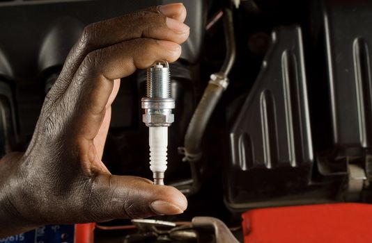 South African or American hand holding car spark plug with modern car engine background