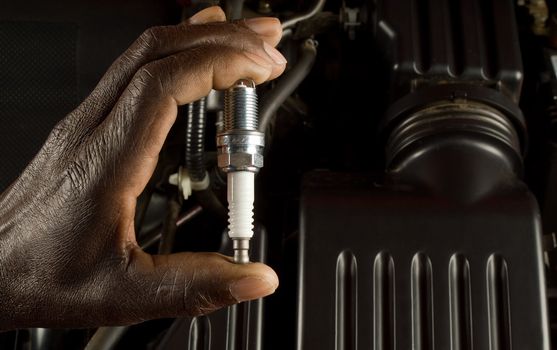 South African or American hand holding car spark plug with modern car engine background