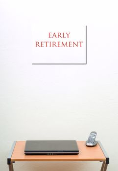 Early retirement sign on wall, office desk, closed laptop with portable phone