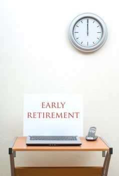 Office desk with early retirement sign on open laptop with portable phone, clock on wall above desk