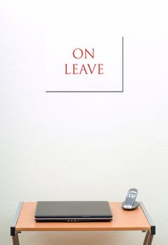 On leave sign on wall behind desk with laptop and portable phone