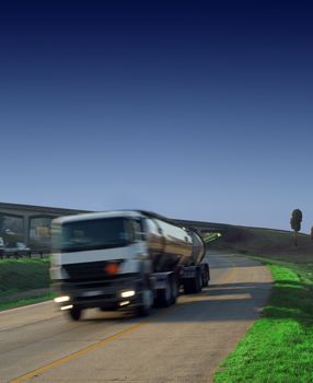 Petrol, diesel or gas tanker truck on highway with green grass and blue sky