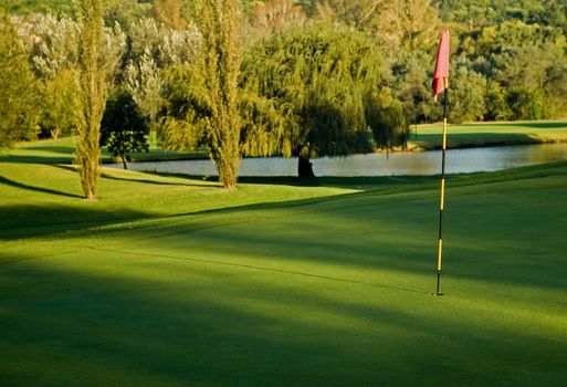 Golf putting green with flag and water hazard pond background