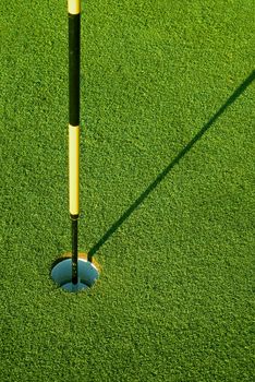 Striped golf flag in green hole with morning shadow on grass