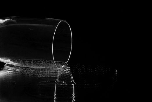 Empty champagne flute lying on it's side reflecting in a mirror with a black background