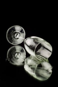 Empty champagne flute lying on it's side reflecting in a mirror with a black background