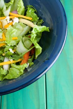 Green salad in blue bowl on wooden table
