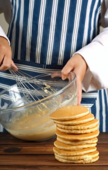 Flapjacks or pancakes in a pile or tower with woman cook or chef mixing pancake or flapjack mixture in background