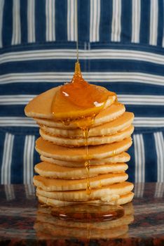 Chef or cook with striped apron pouring syrup on flapjacks or pancakes