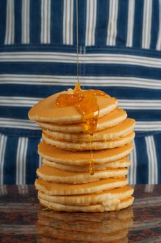 Chef or cook with striped apron pouring syrup on flapjacks or pancakes