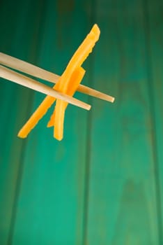 Chopsticks holding two yellow peppers over wooden table