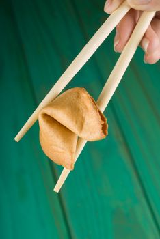 Chopsticks holding fortune cookie over green table