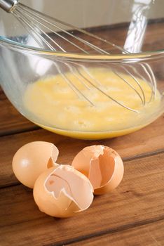 Cooking making pancake mixture with broken used egg shells and pancake batter in background with whisk