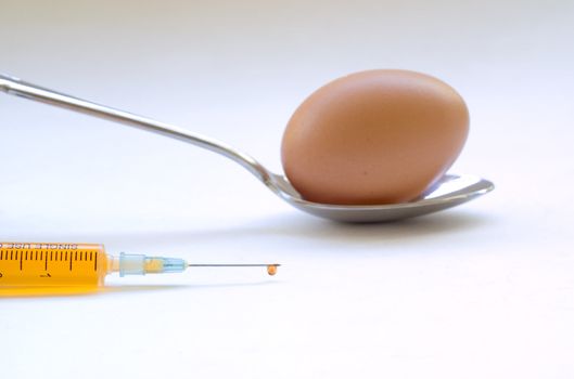 Genetic modification food concept of egg on spoon with medical injection and needle with orange fluid
