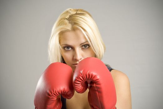 Portrait of pretty fit blond woman boxer training or working out with red boxing gloves