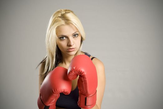 Fighting pretty fit blond woman boxer training or working out with red boxing gloves