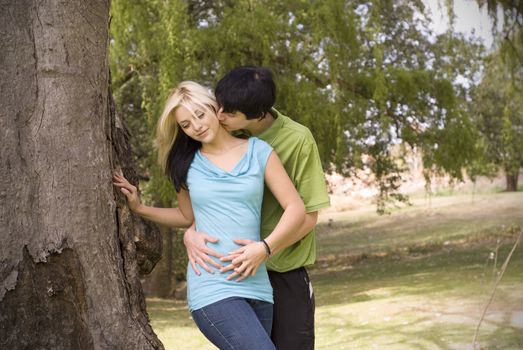 Boyfriend kissing girlfriend neck next to brown garden tree