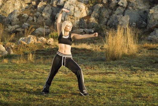 Pretty woman praticing exercise tai chi, kung fu or yoga in natural park with gold light reflector