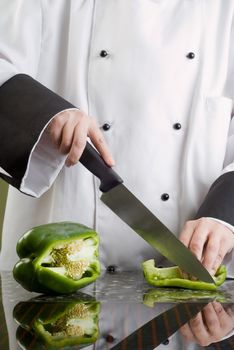Chef in Black and White Uniform Cutting a Green Pepper Reflecting in Stove Top