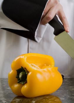 Chef in Black and White Uniform Cutting a Yellow Pepper Reflecting in Stove Top