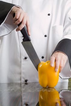 Chef in Black and White Uniform Cutting a Yellow Pepper Reflecting in Stove Top