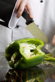 Chef in Black and White Uniform Cutting a Green Pepper Reflecting in Stove Top