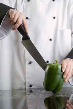 Chef in Black and White Uniform Cutting a Green Pepper Reflecting in Stove Top