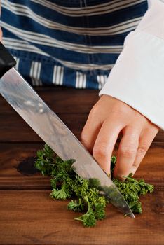 Woman cook or chef chop or chopping parsley with knife on wooden board