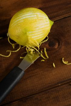 Zesting or sested lemon on wooden table with kitchen implement