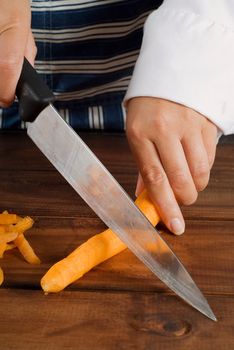 Woman female cook or chef slicing or cutting a carrot with kitchen knife on wooden board