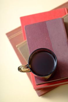 Pile of old books with covers and white pages with red background and a mug or cup of coffee