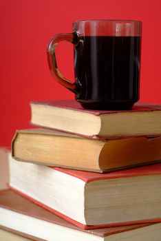 Pile of old books with covers and white pages with red background and a mug or cup of coffee