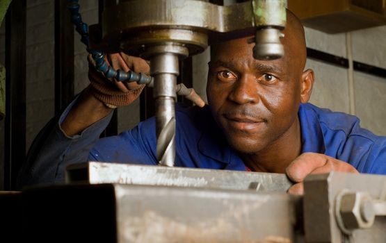 South African or American worker engineer working with industrial drill press