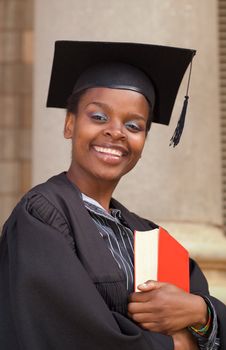 Graduating African American college student on campus with book and mortar board