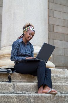 African American college student with laptop on library steps