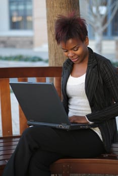 African American businesswoman sitting on outside bench with laptop