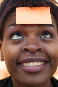 Smiling African American businesswoman with post it reminder note on forehead - focus on eyes