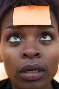 Confused African American businesswoman with post it reminder note on forehead - focus on eyes