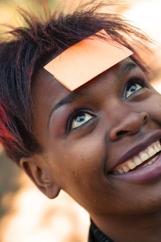 Smiling African American businesswoman with post it reminder note on forehead - focus on eyes