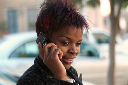 Smiling happy African American businesswoman talking on cell phone in front of new cars - arranging for finance