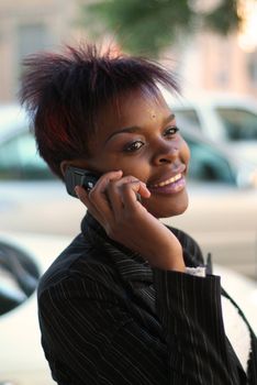 Smiling happy African American businesswoman talking on cell phone in front of new cars - arranging for finance