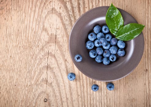 Fresh blueberries in bowl with leaves on wooden background with copy space. Top view