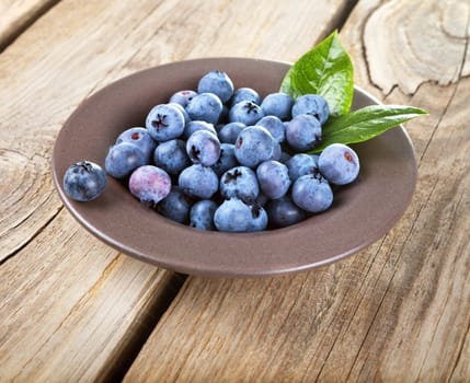 Fresh blueberries in bowl with leaves on wooden background