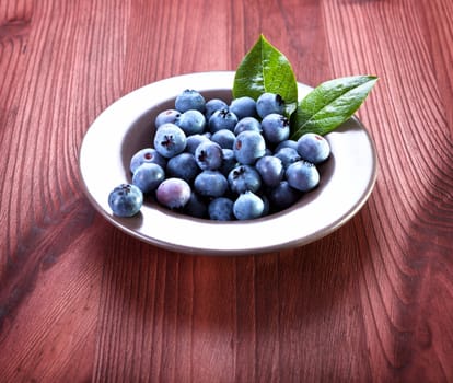 Fresh blueberries in bowl with leaves on wooden background