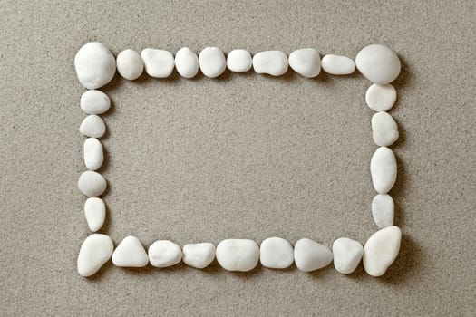 Frame of white pebbles on sand background with copy space