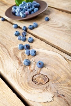 Fresh blueberries with leaves in brown bowl. Some blueberries spilled on wooden background