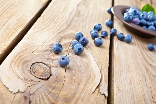 Fresh blueberries with leaves in brown bowl. Some blueberries spilled on wooden background