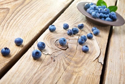 Fresh blueberries with leaves in brown bowl. Some blueberries spilled on wooden background